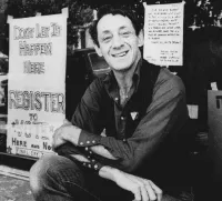 Harvey Milk Sitting in Front of Register to Vote Signs