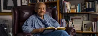 Nikki Giovanni Sits in a Chair With a Book in Her Home
