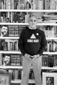 Larry Kramer at Home Wearing a Silence = Death Shirt Standing in Front of His Book Collection in 1989
